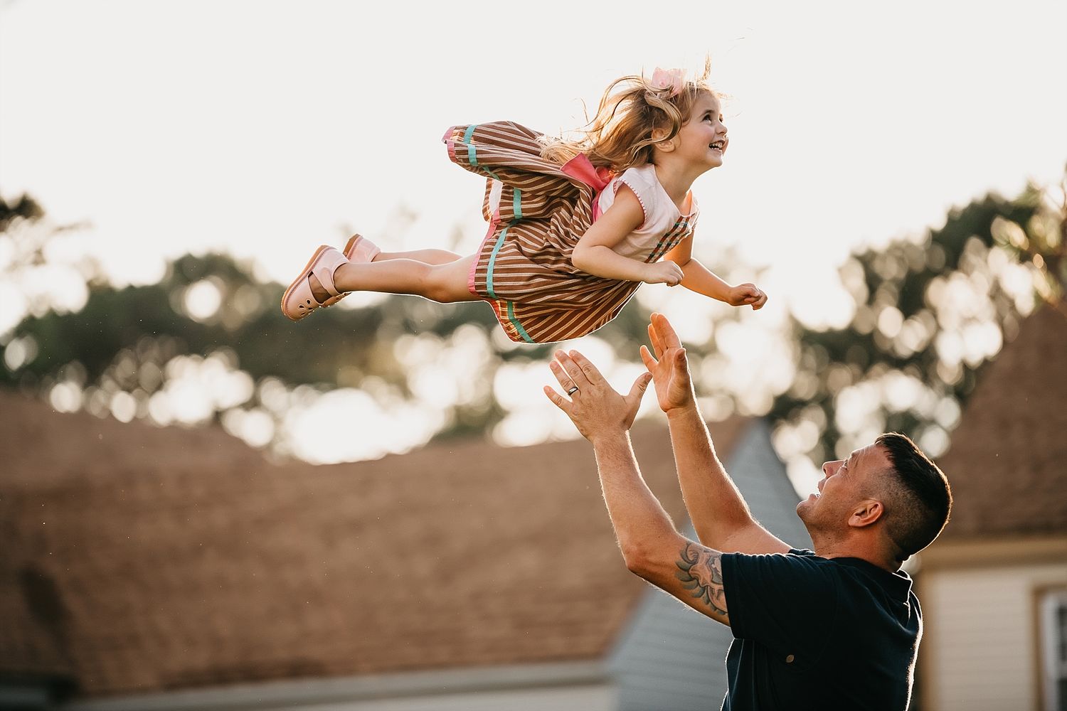 Playful moment captured as child is lifted high into the air outdoors.