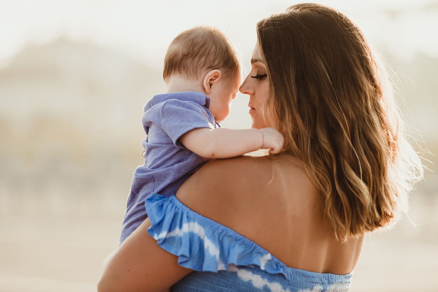 A tender moment between parent and baby against a bright outdoor backdrop.