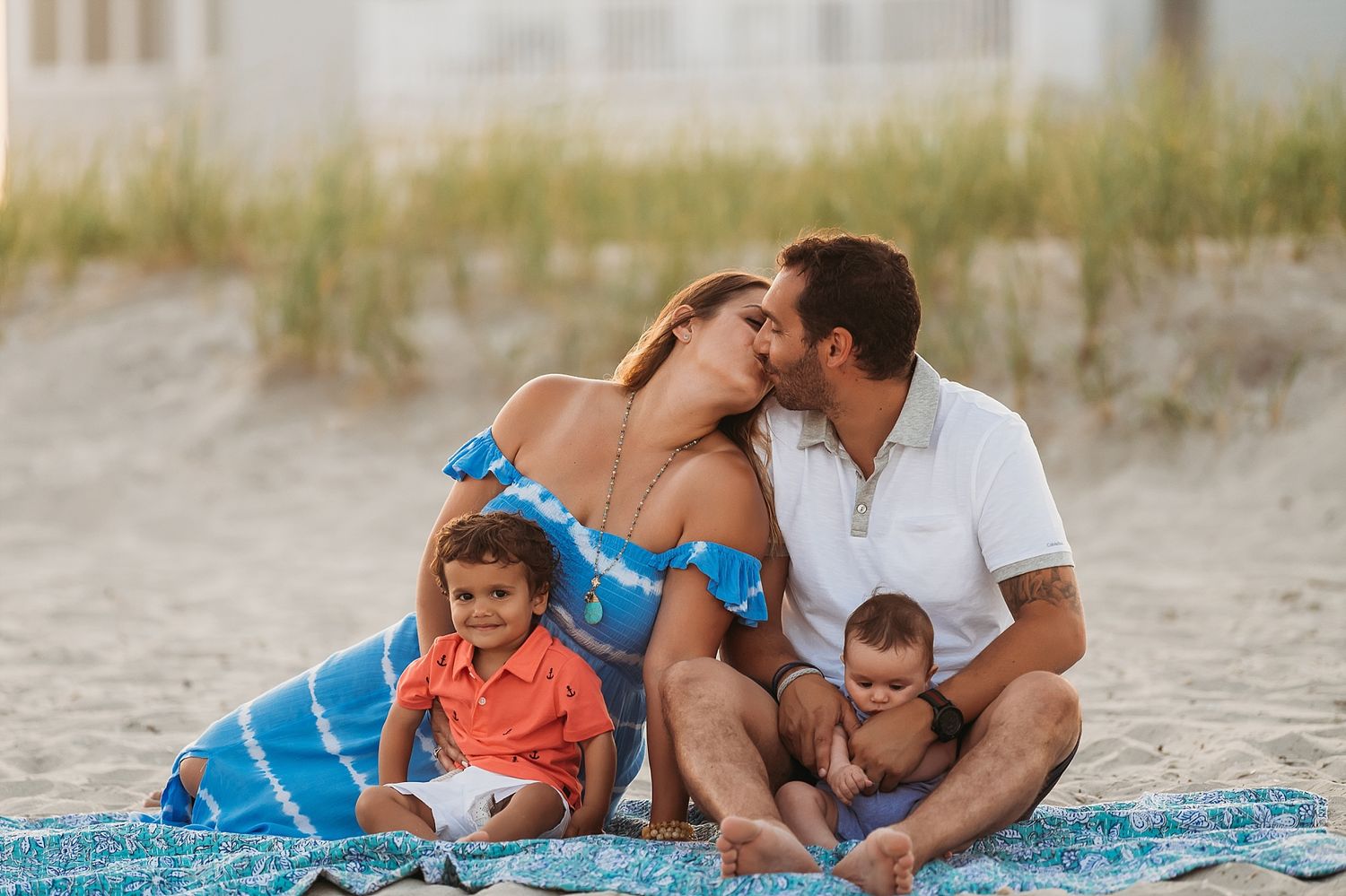 A family sits together on a blanket at the beach during sunset.