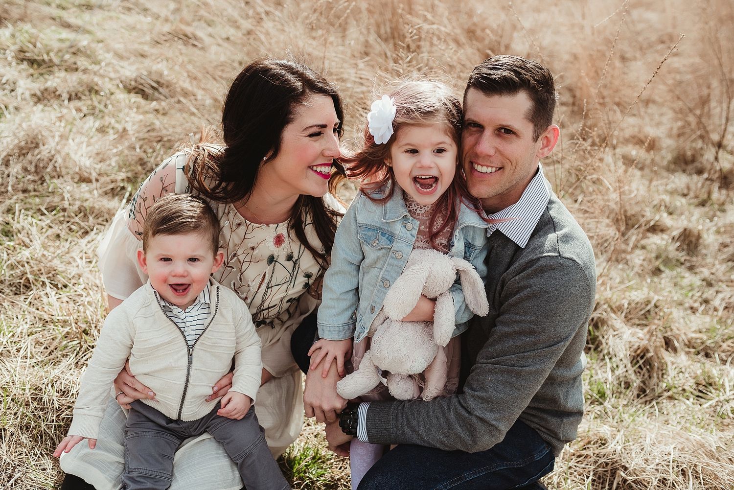 A happy family poses together in a field while holding a white bunny.