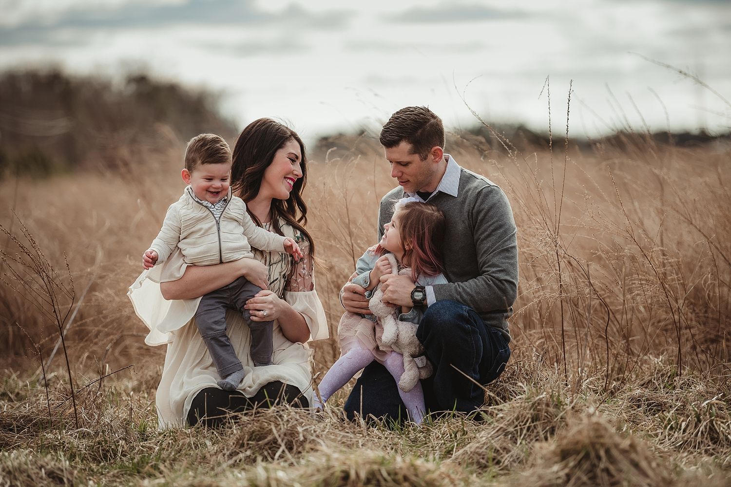 A family sits together in tall grass during an outdoor photo session.