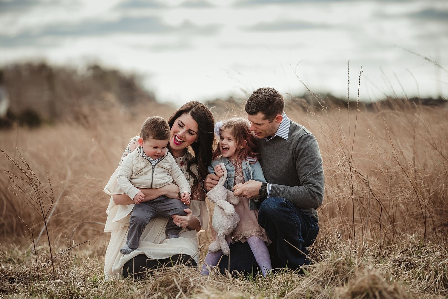 A family sits together in a field of tall grass during an autumn photoshoot.