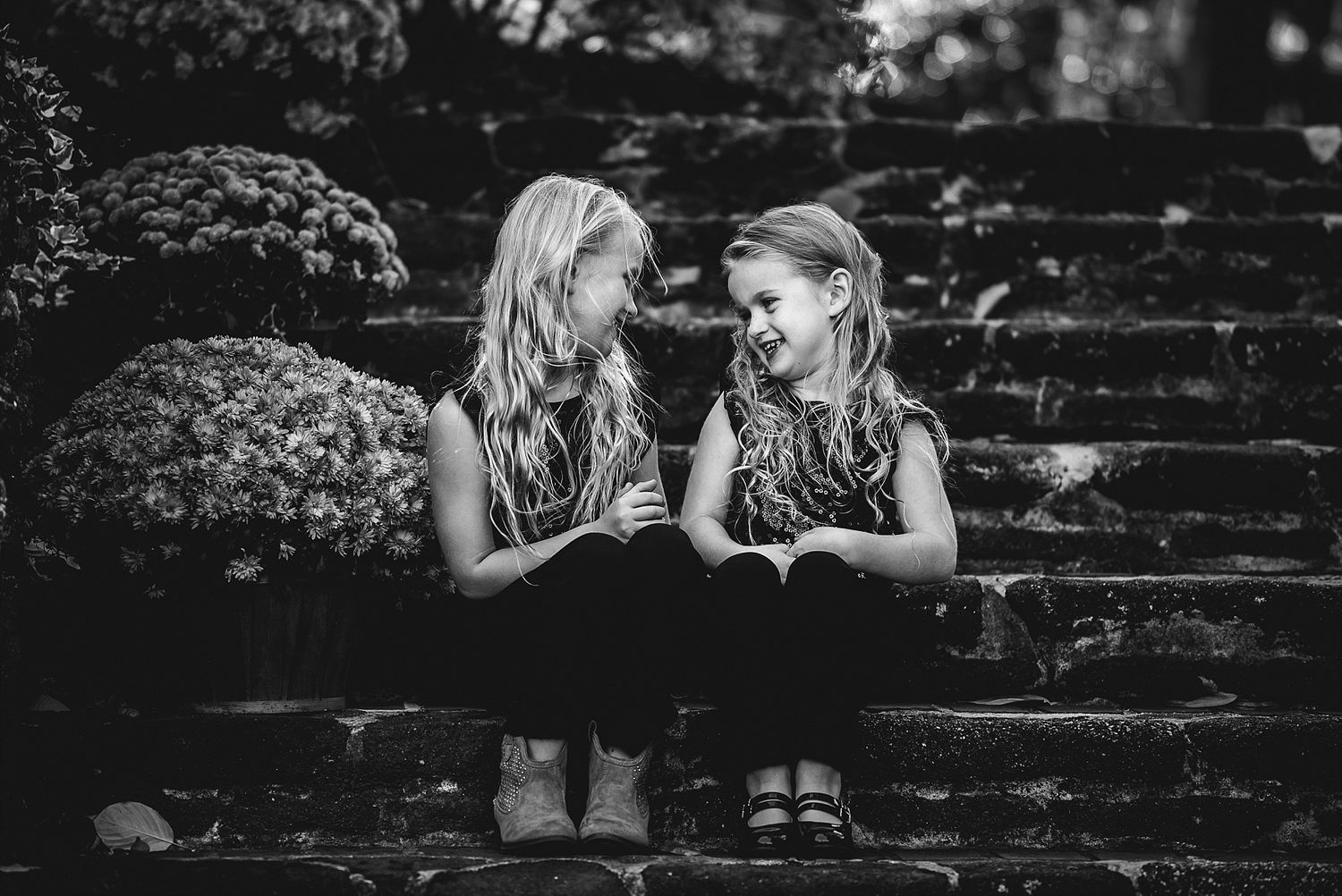 Two children sit on stone steps having a conversation in black and white.
