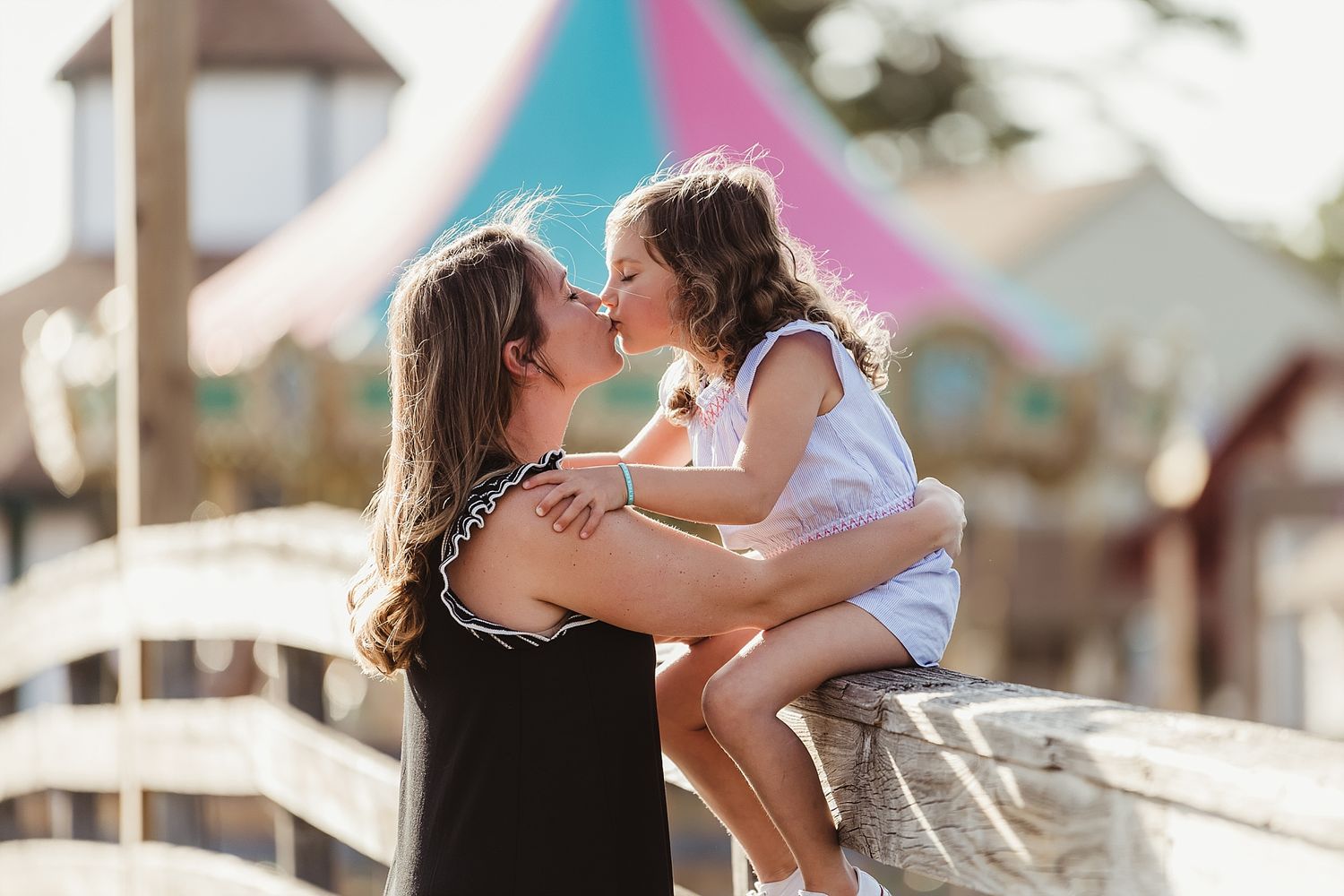 A tender moment between parent and child against a colorful carnival backdrop on a sunny day.