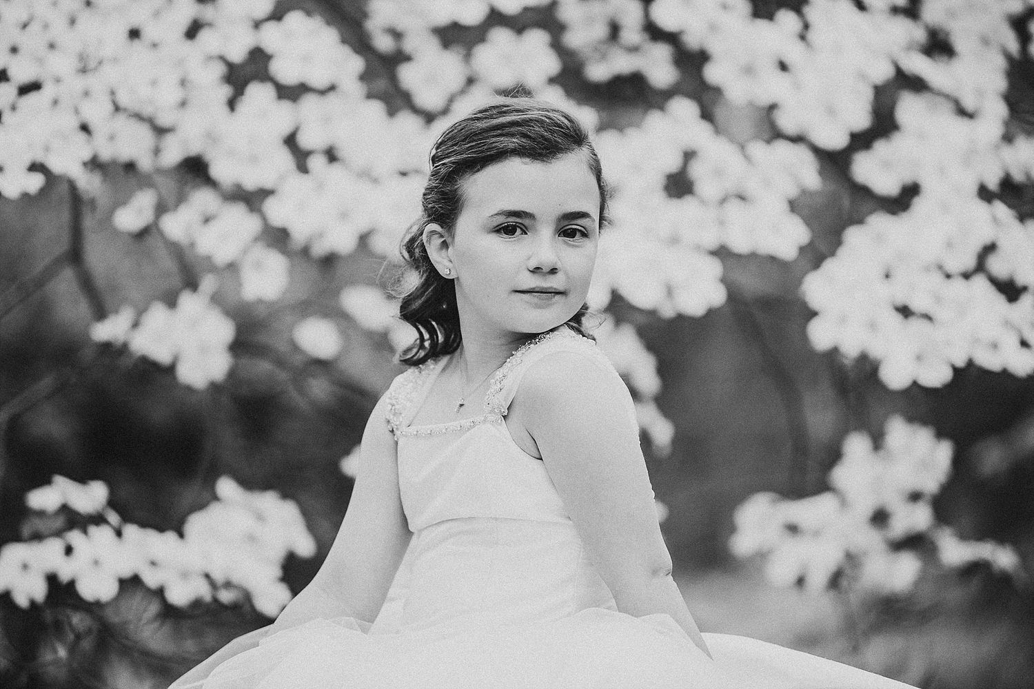 Black and white portrait amid blossoming flowers capturing elegance in a formal dress.