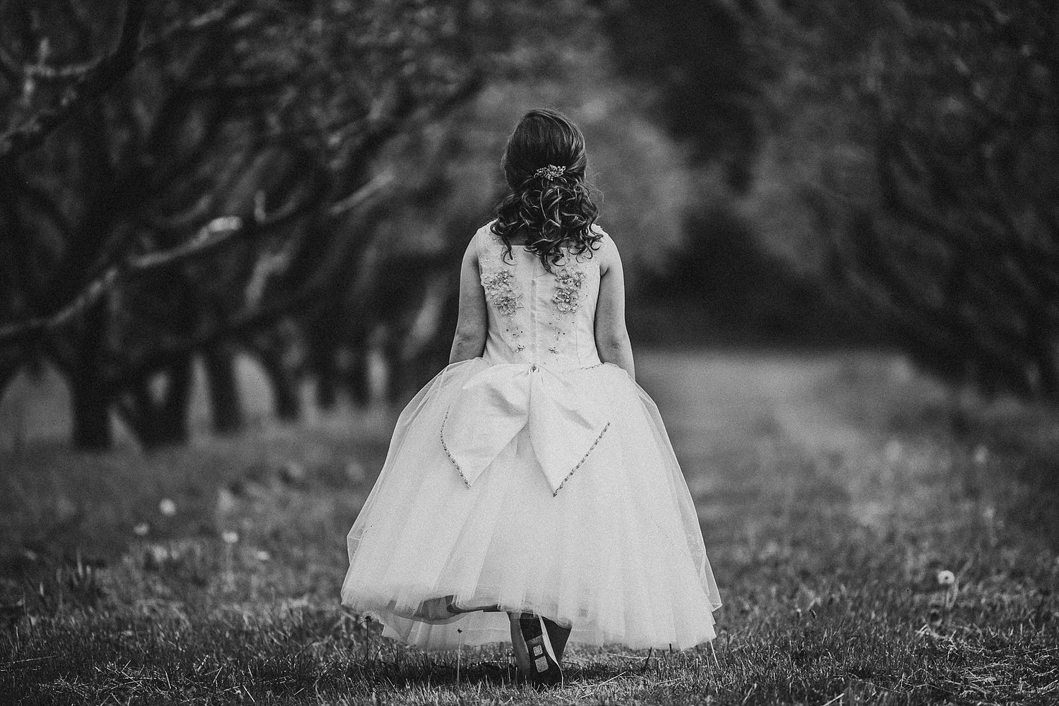 Romantic black and white portrait in a formal dress along a tree-lined path.