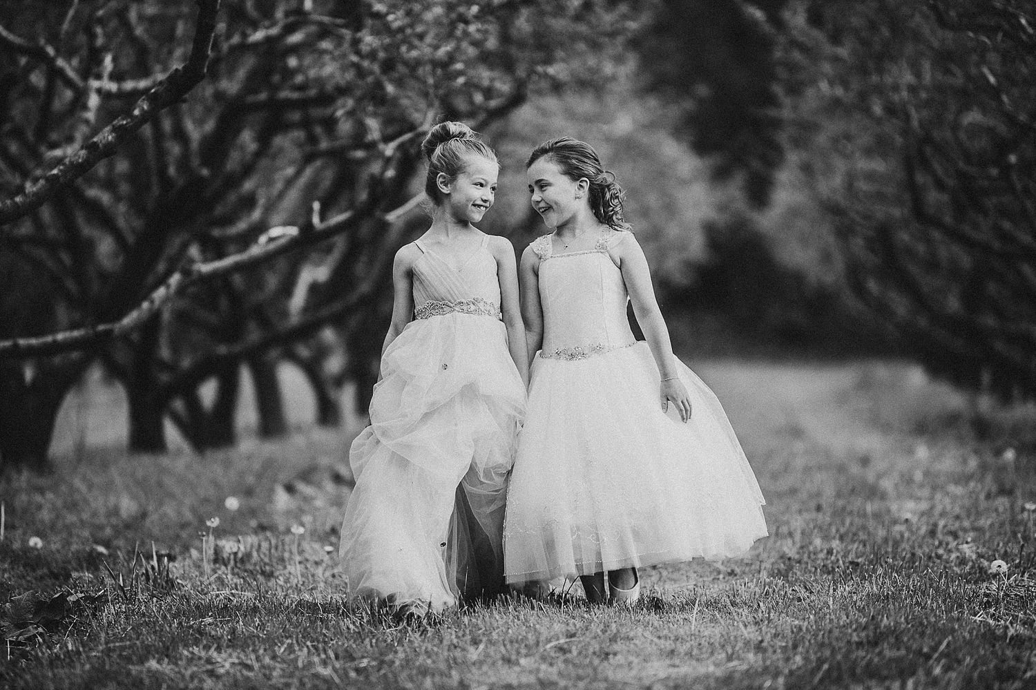 Black and white photo of two formal dresses walking together in an orchard setting.