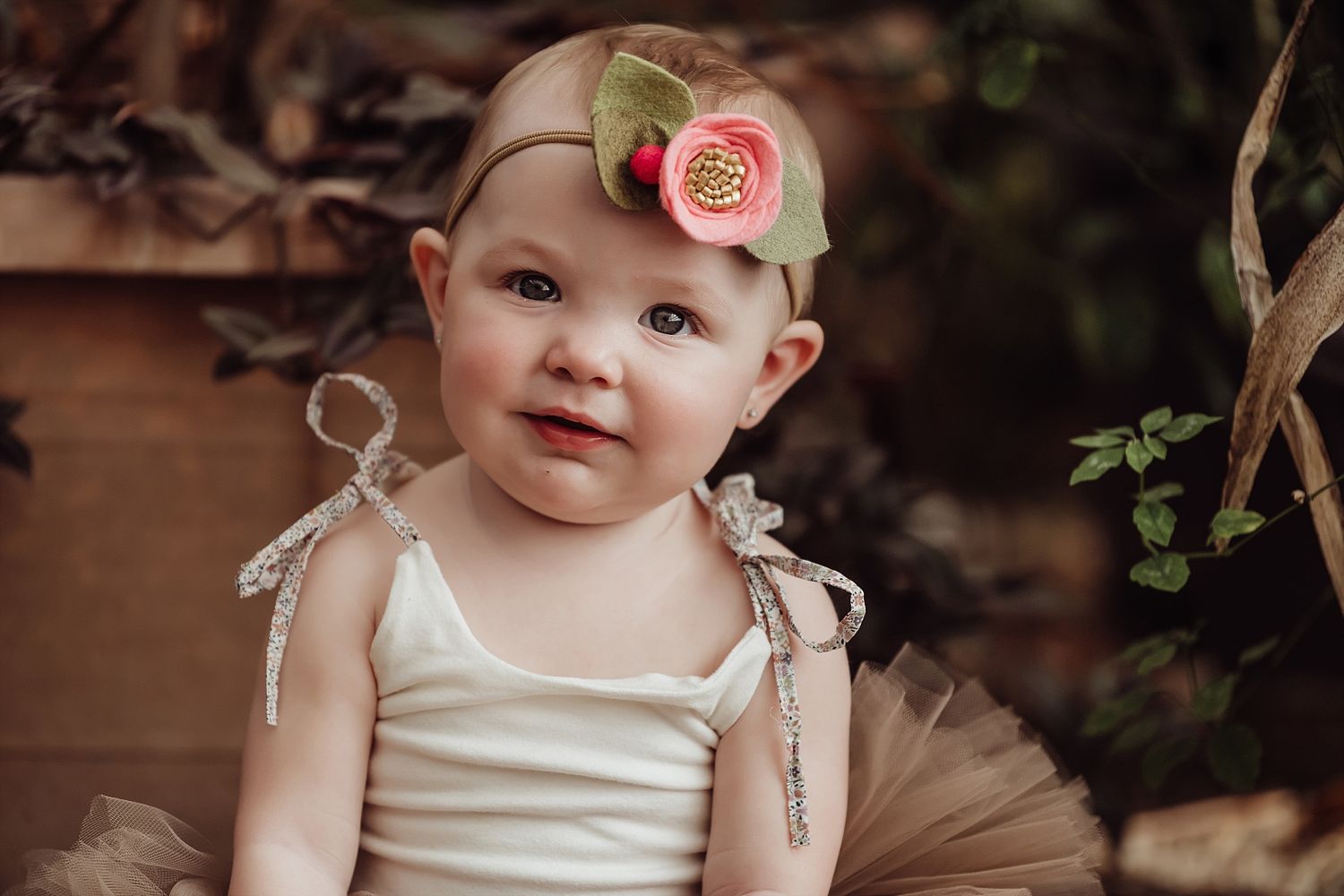 Baby wearing a tulle dress and floral headband poses with a sweet smile.