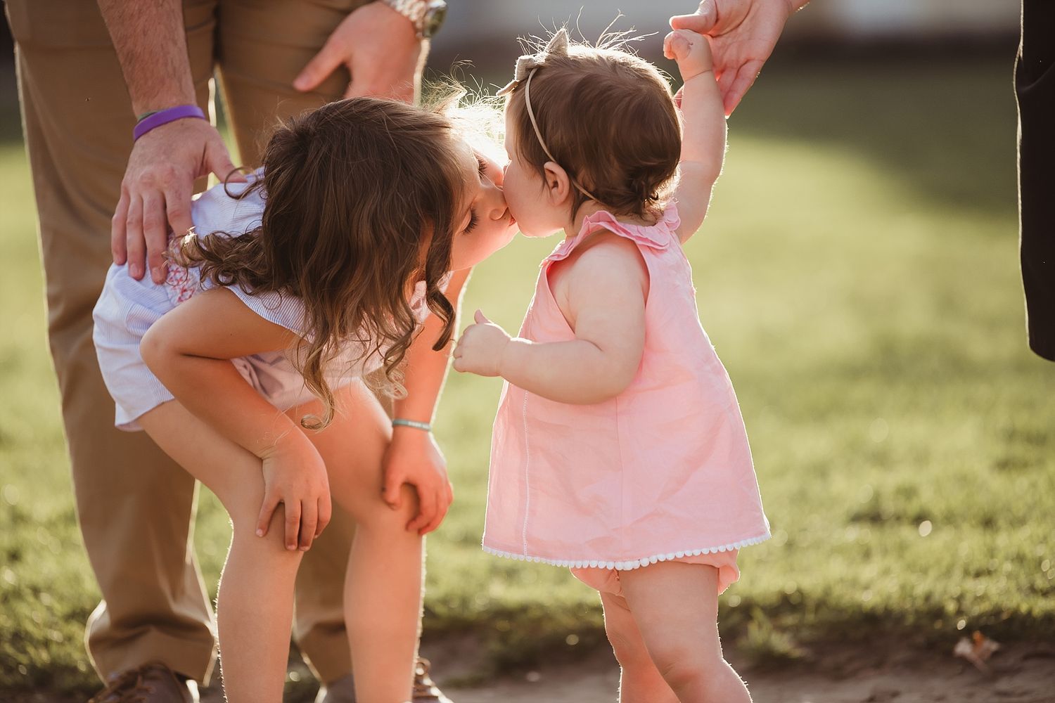 Two small children playing and sharing a sweet moment together in warm sunlight on grass.