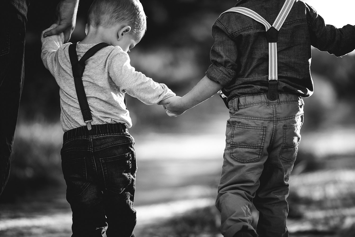 A black and white image capturing a tender moment between two small figures holding hands.