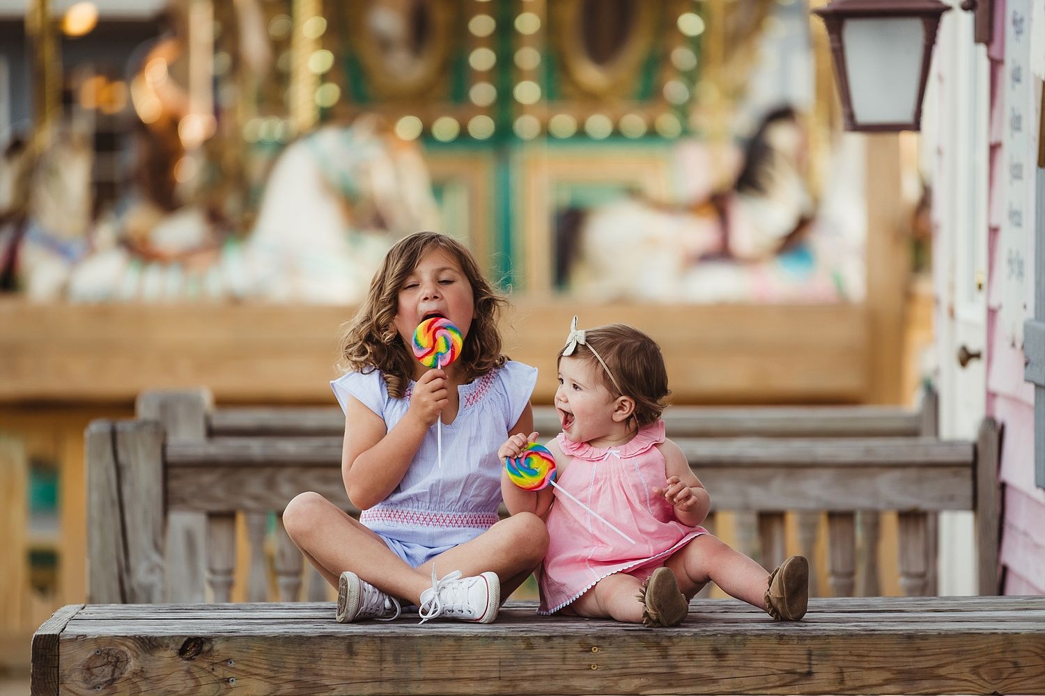 Two children sitting together on wooden steps at a carnival, sharing a playful moment.