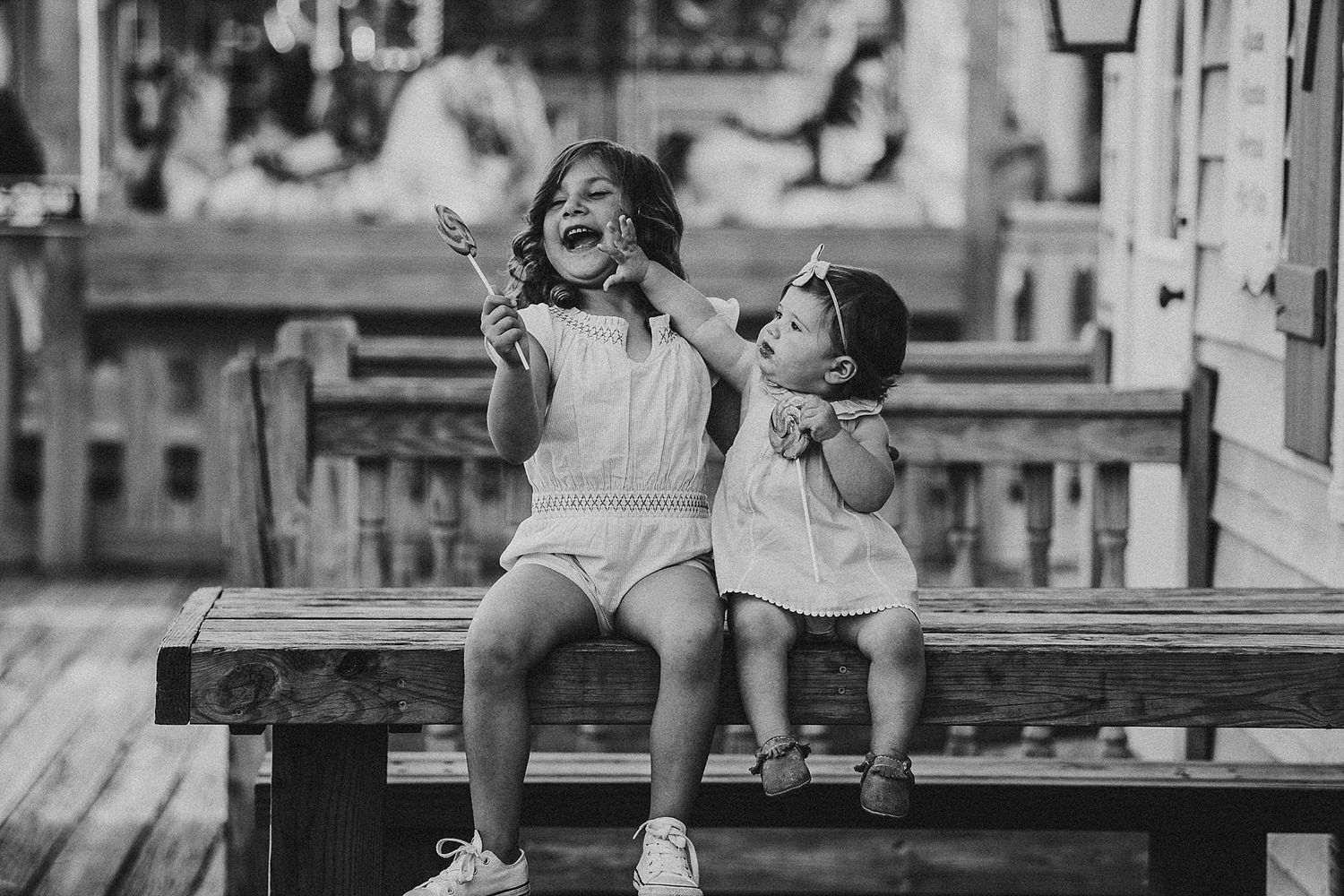 Two children sitting on wooden bench eating ice cream in black and white photography.