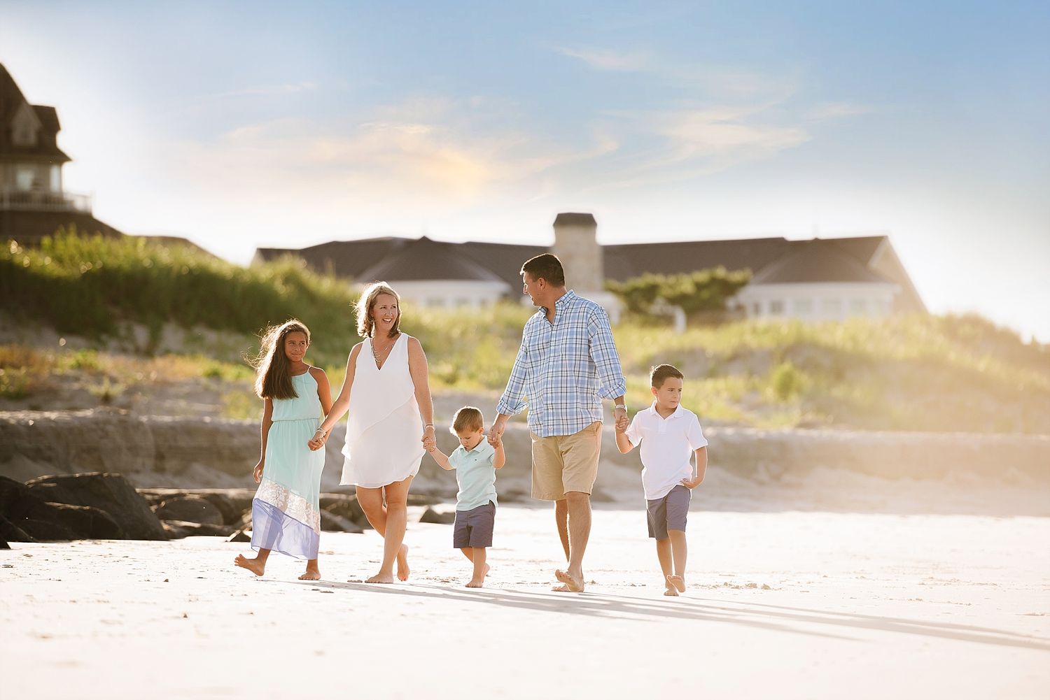 Family walking together on beach at sunset creating silhouettes against golden sky.