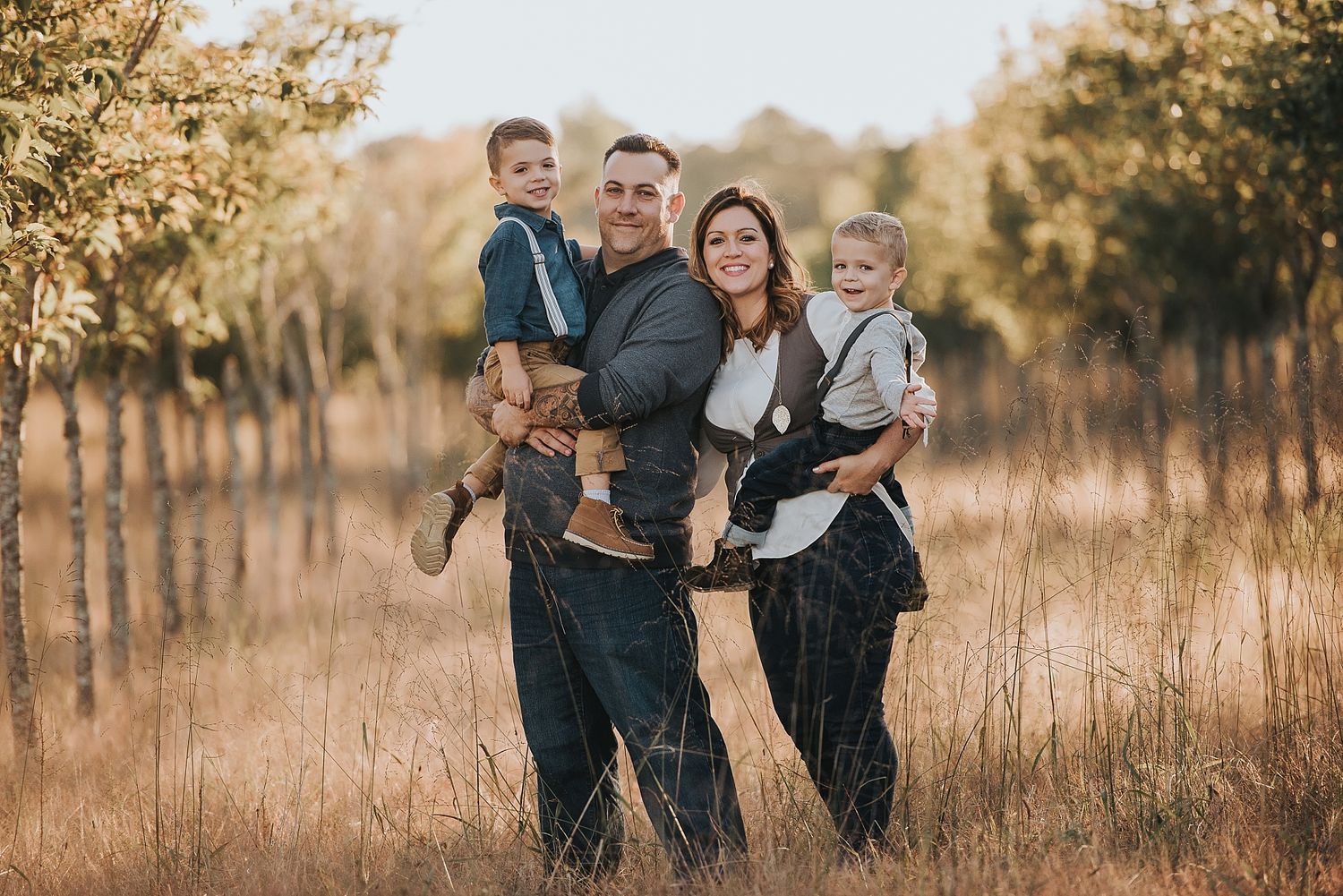Family portrait of four people standing together in a sunlit autumn field at golden hour.