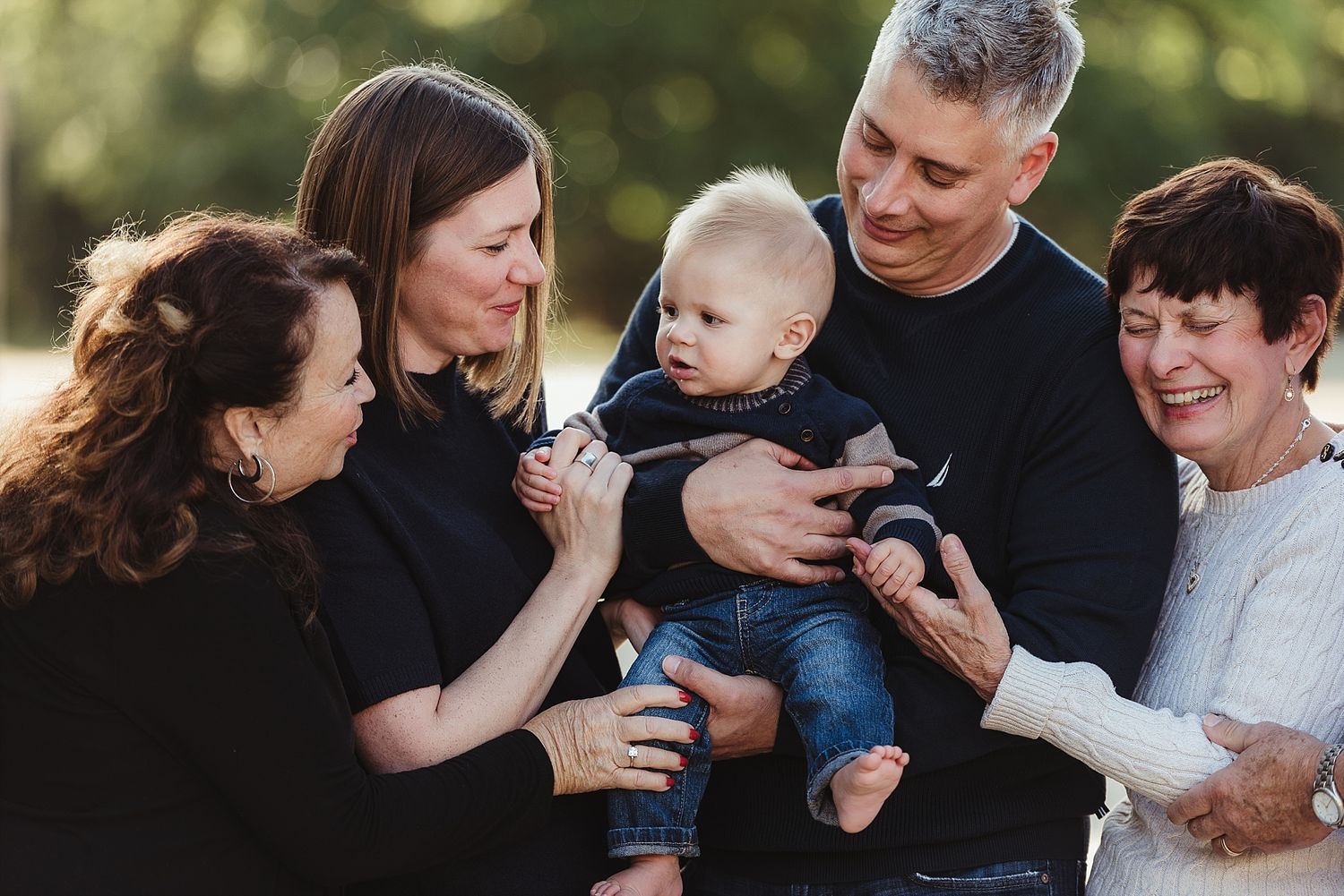 Multi-generational family gathering outdoors sharing joyful moment with infant.