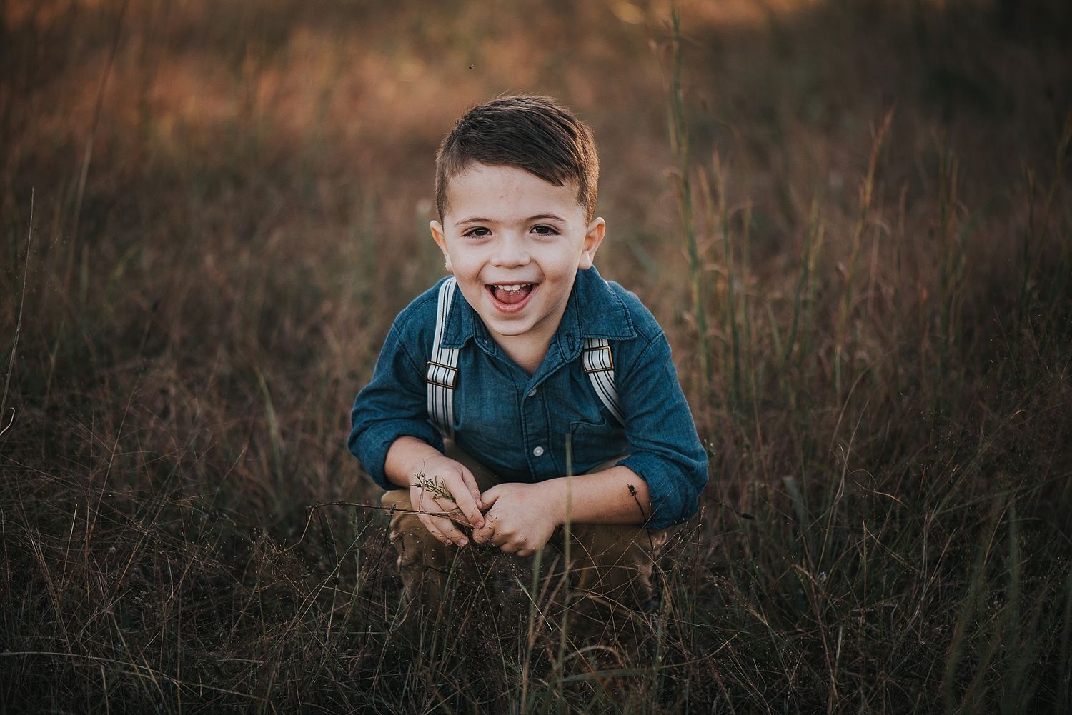 Young person lying in tall grass at sunset smiling at camera.