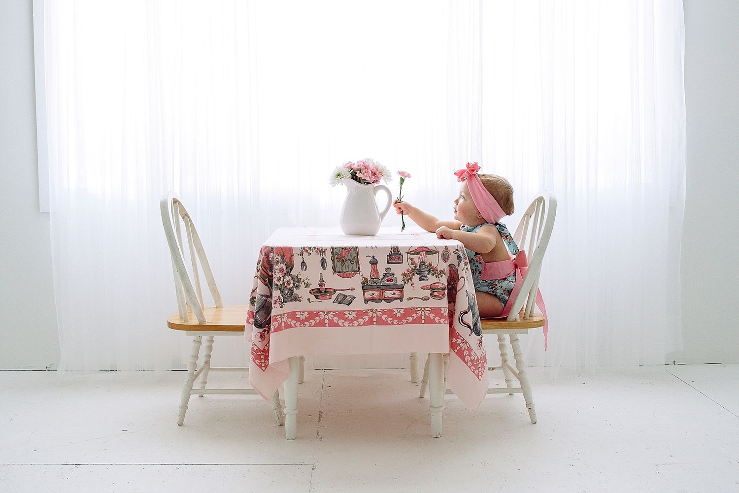 Tea party setup with vintage table settings and chairs in bright white room.