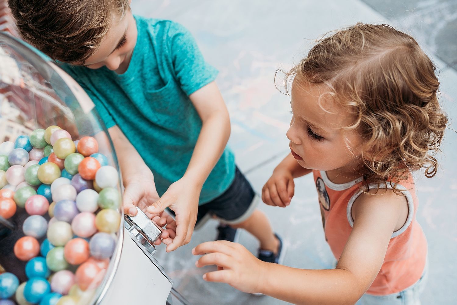 Children playing with colorful gumball machine filled with bright candy balls.