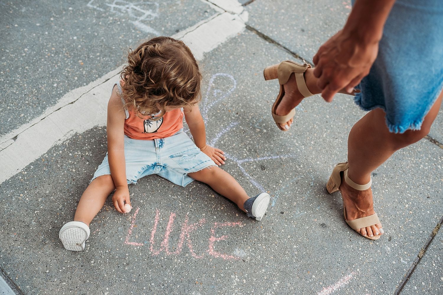 Child drawing with chalk on sidewalk while being supervised.