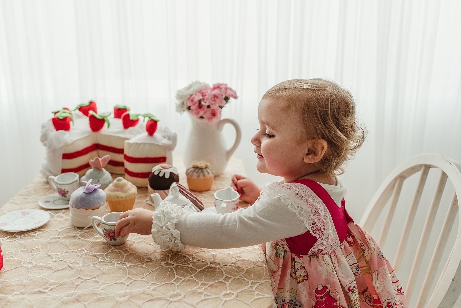 Toddler at elegant tea party table with strawberry desserts and pink flowers.