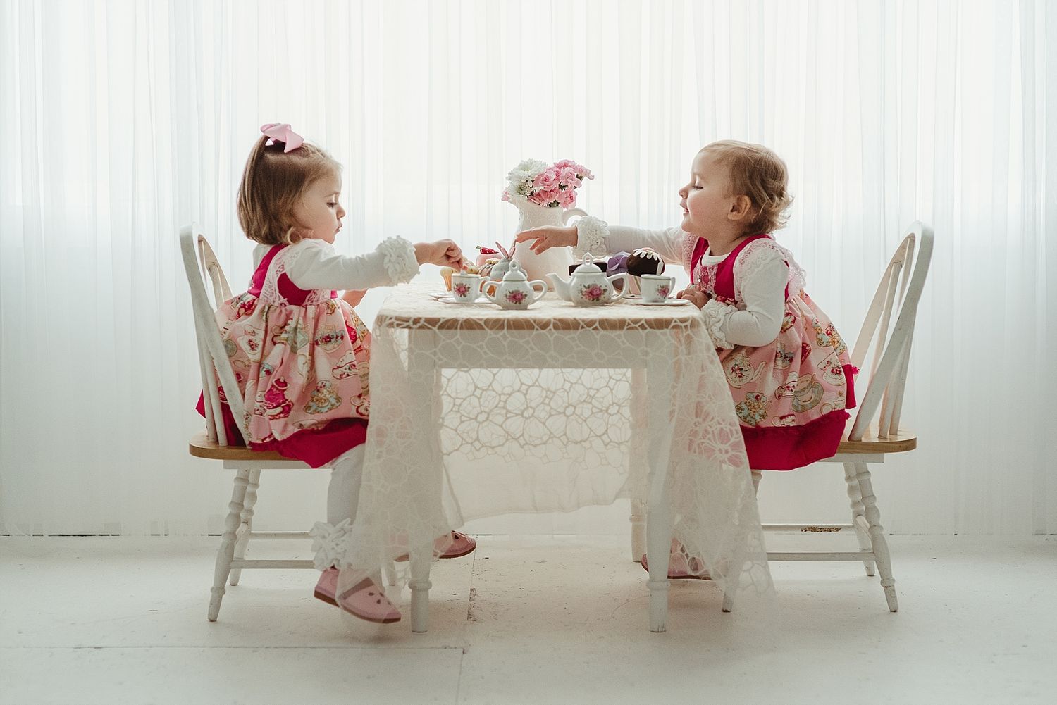 Children having fancy tea party at white table with matching outfits.