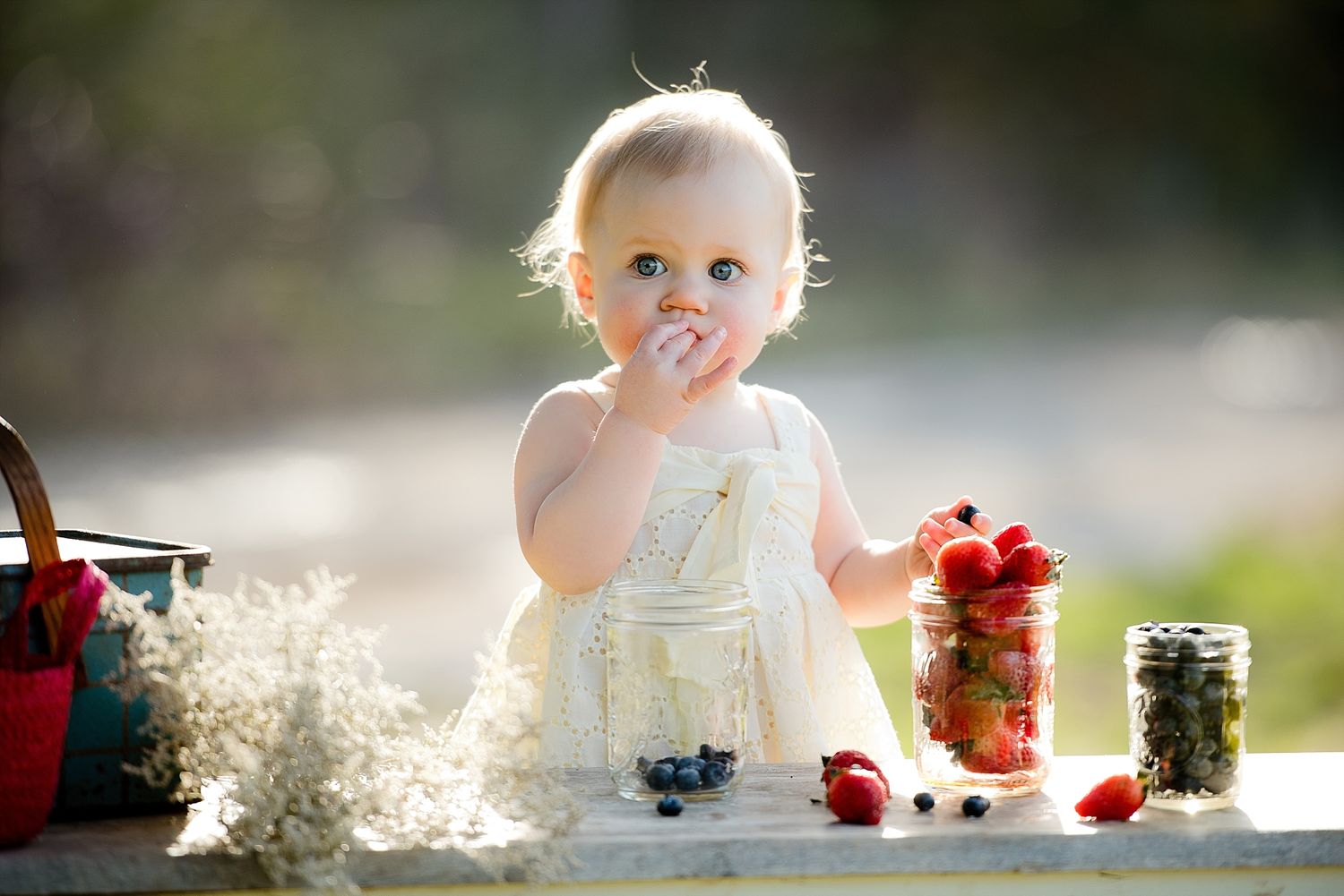 Toddler enjoying fresh berries at outdoor table with jars and baskets.