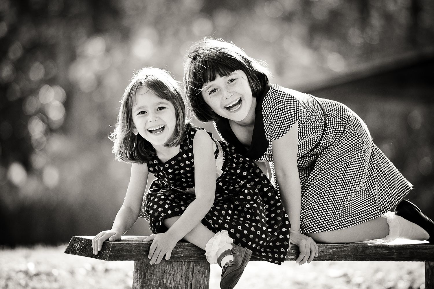 Two figures in polka dot dresses share a happy moment on a bench in black and white.
