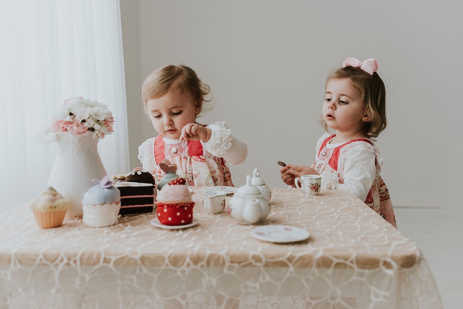 Young children having a fancy tea party with cakes and treats at a white table.