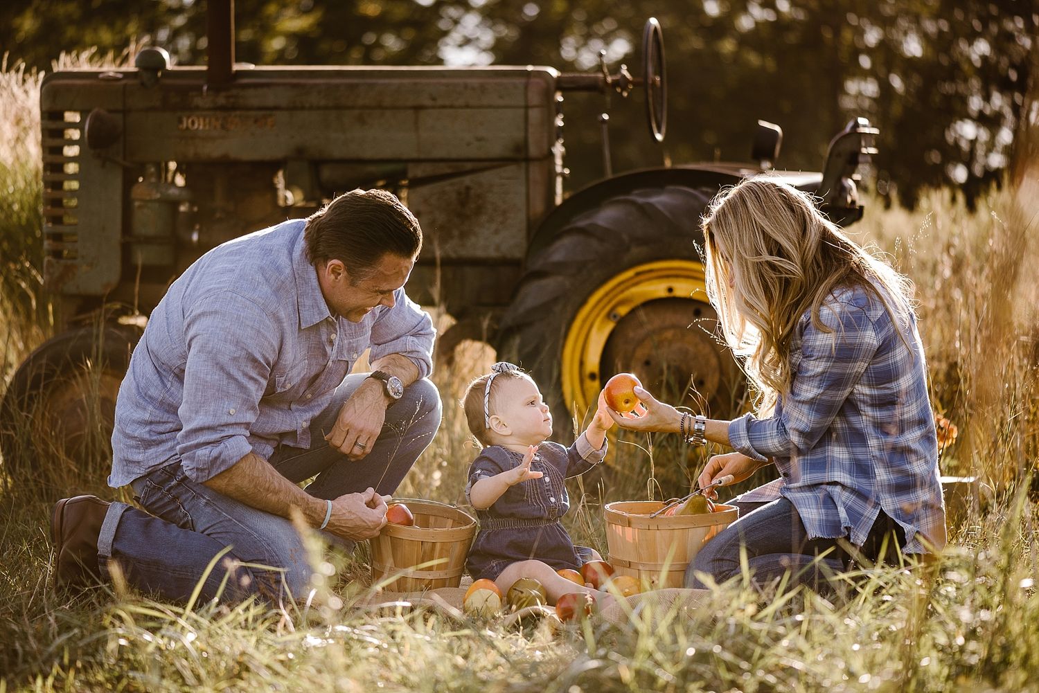 Family sits together by vintage tractor in golden sunset field.