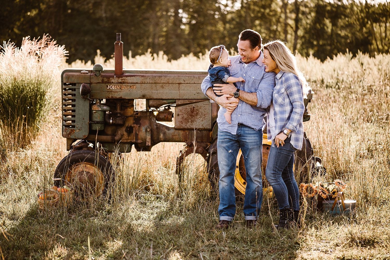 Family poses together by rustic tractor in golden sunset field.