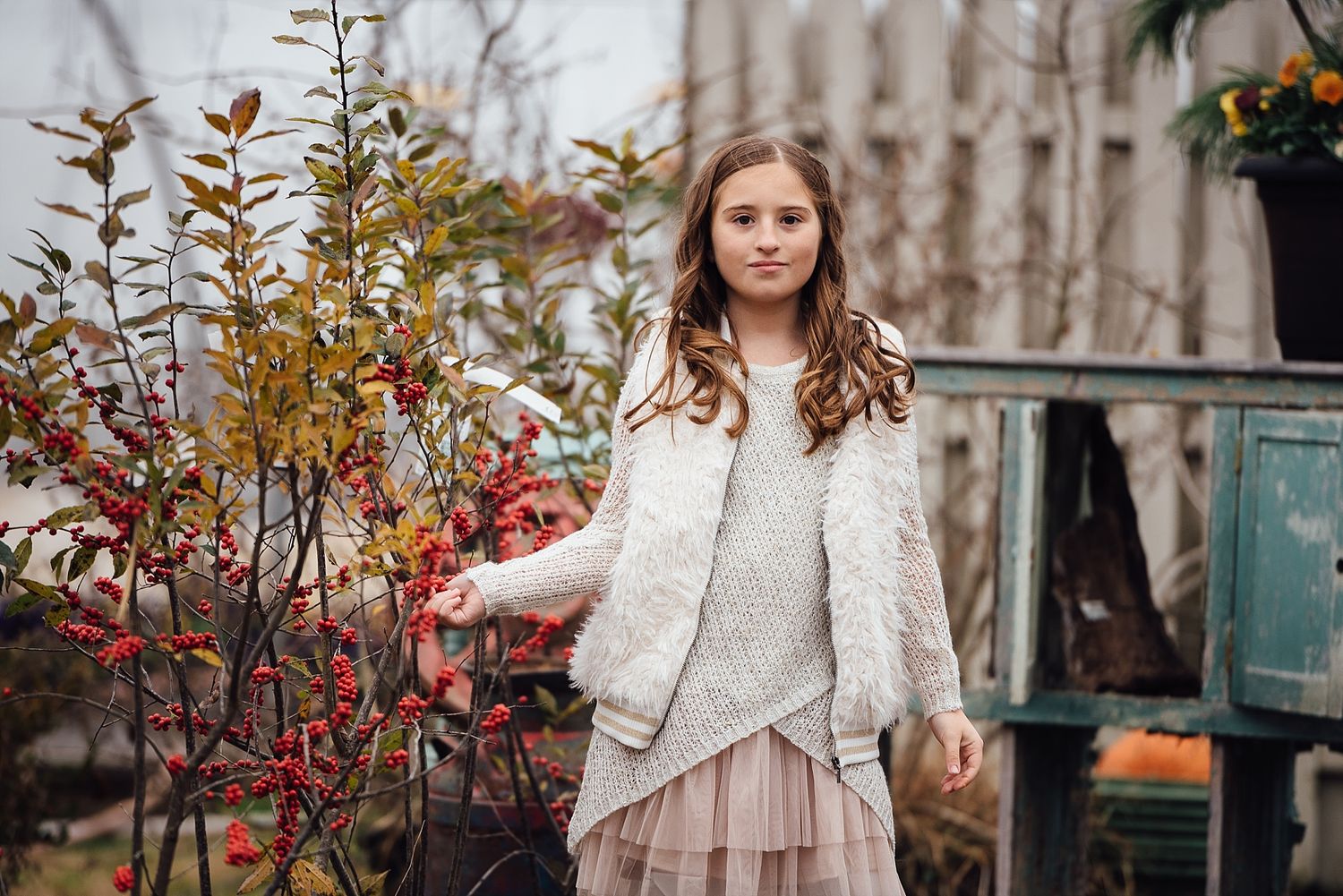 Young person in white sweater and skirt stands by autumn foliage.