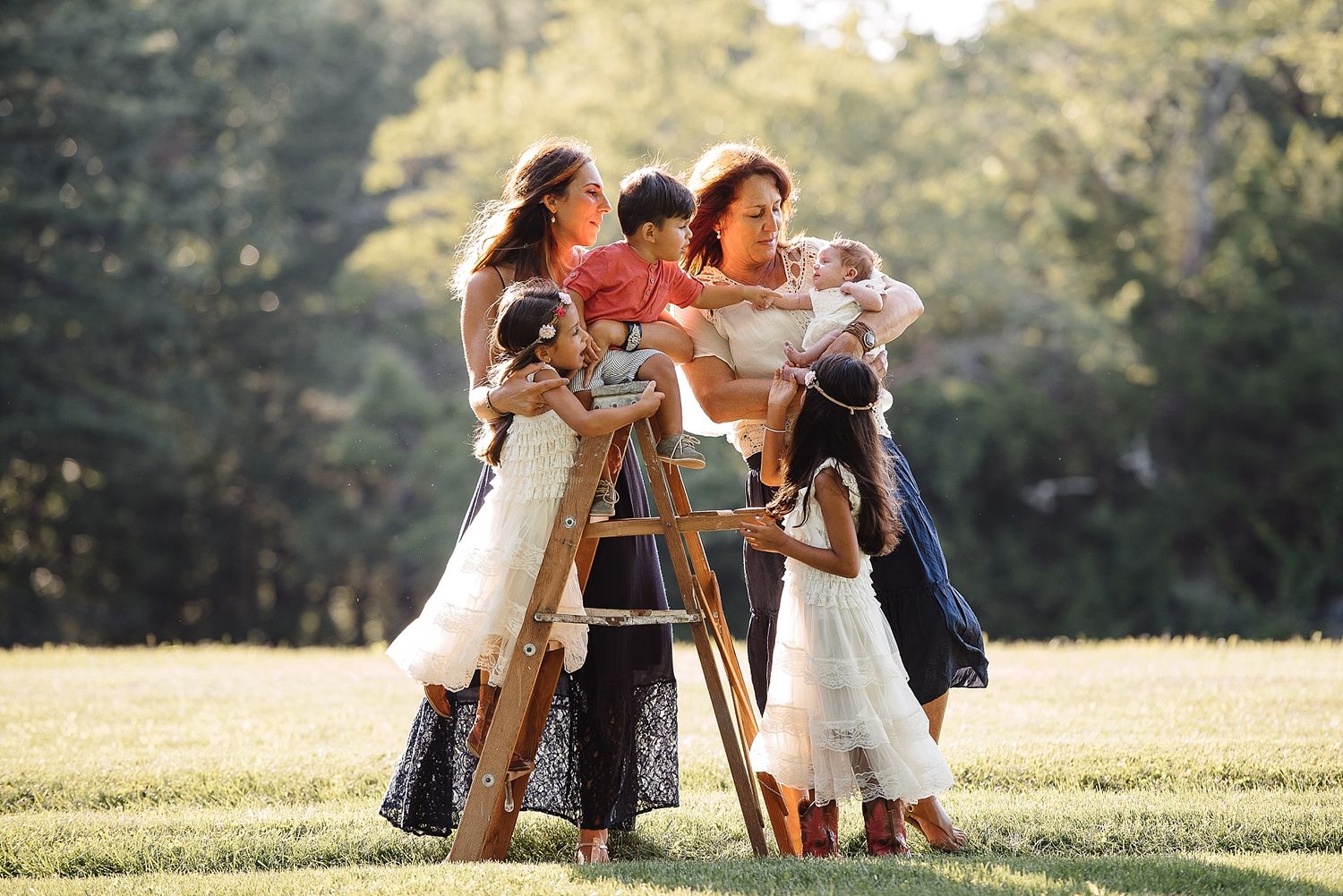 Group gathered on wooden ladder outdoors during golden hour photo session.