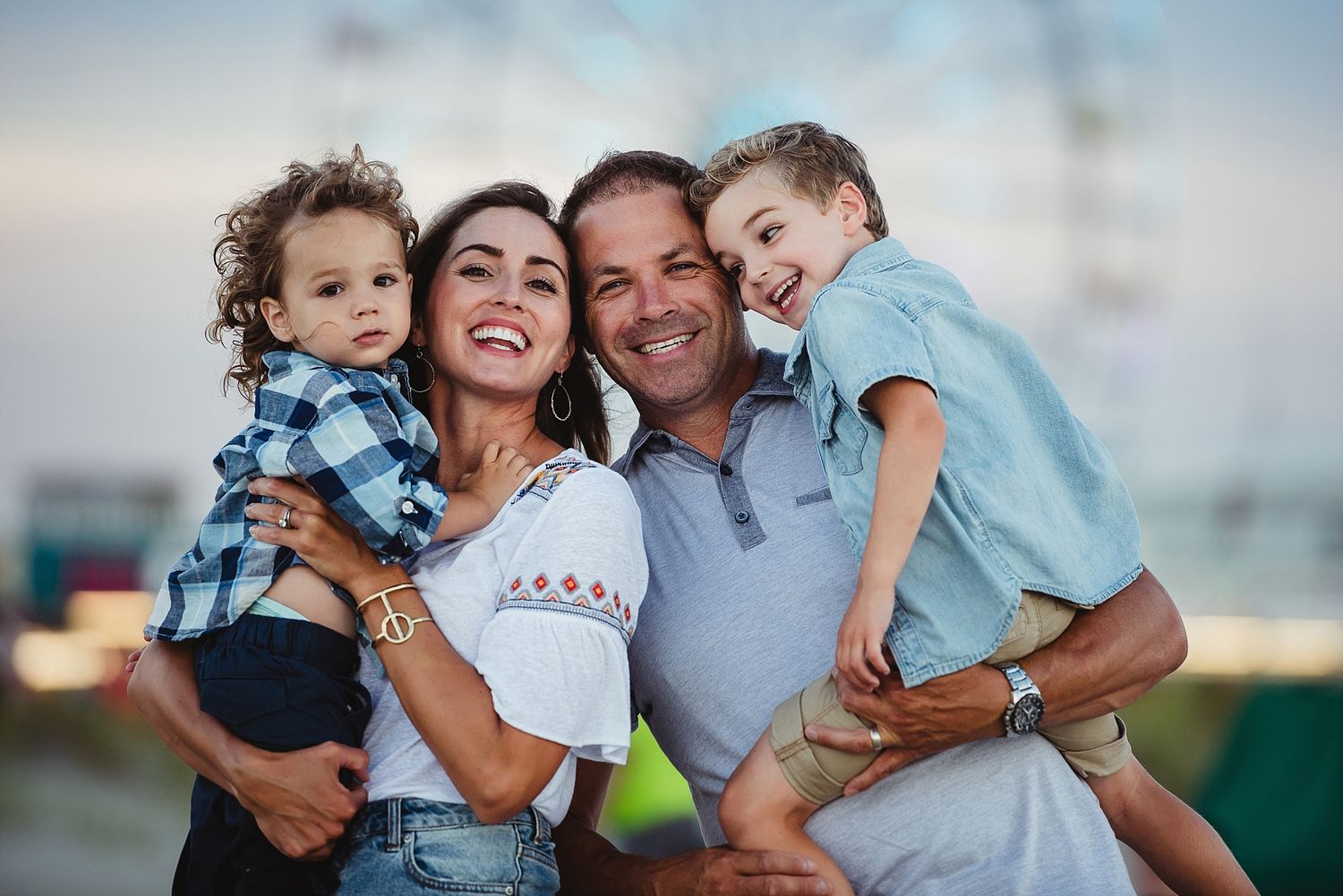 A joyful family of four embraces and laughs together during an outdoor photo session at sunset.