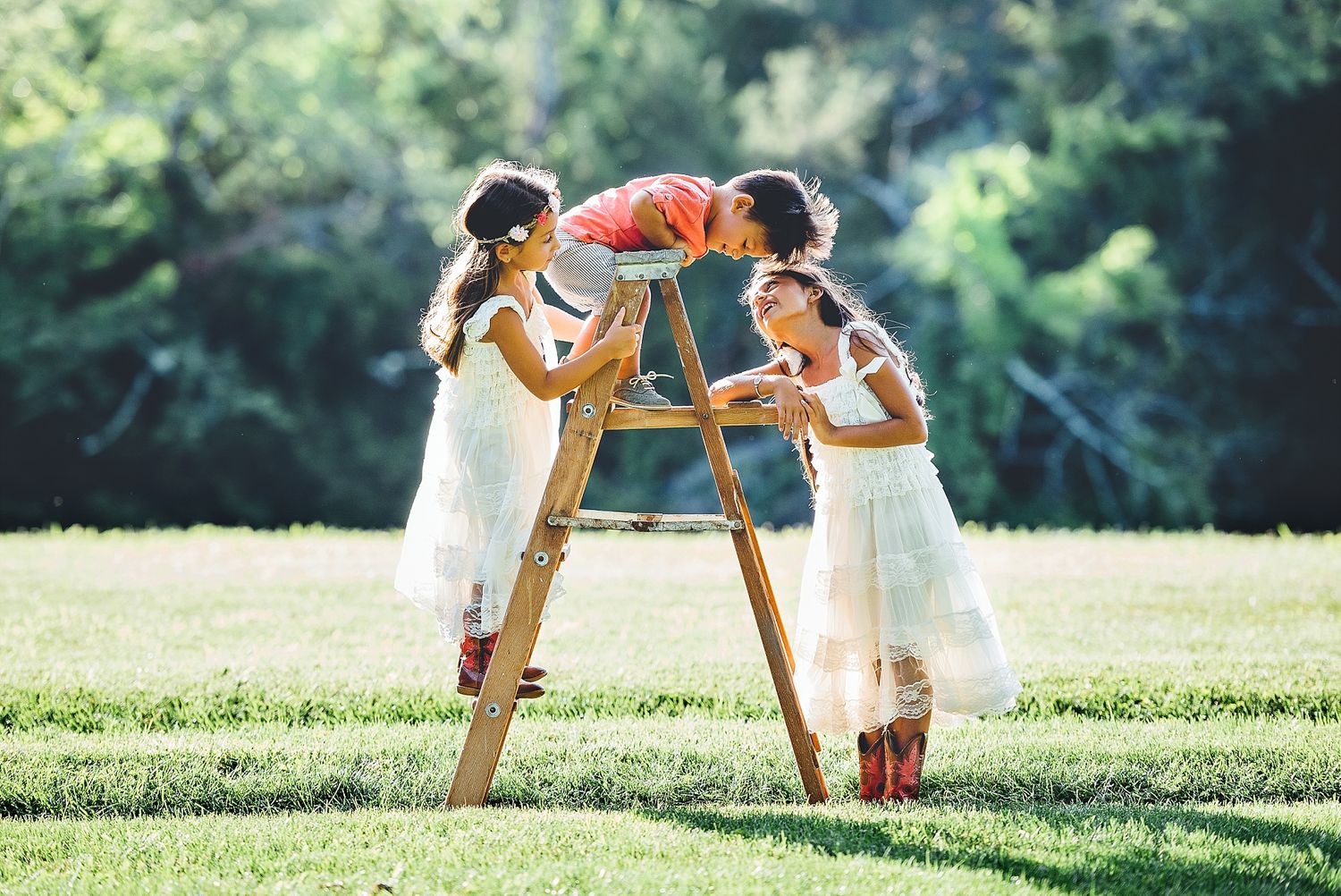 Two children play together on a wooden ladder in a sunny garden setting.