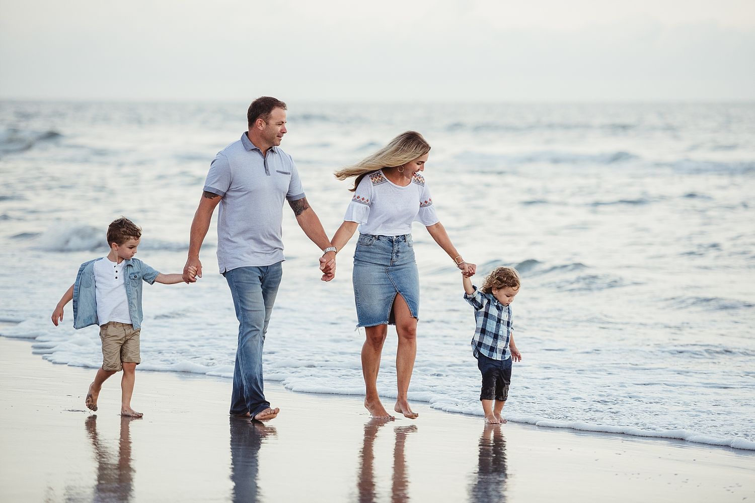 A family walks together along the beach shoreline during sunset.