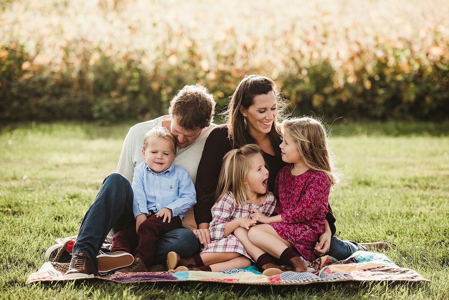 A group shares laughter while sitting together on a blanket in a sunny field.