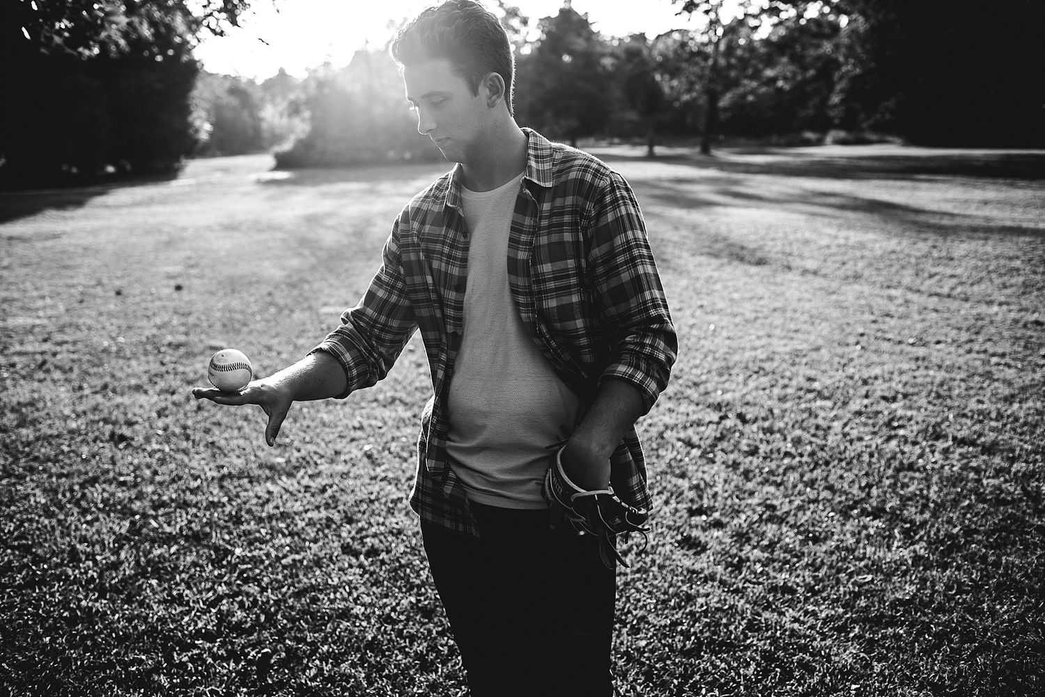 A person in plaid shirt stands in backlit sunlight on grassy field.