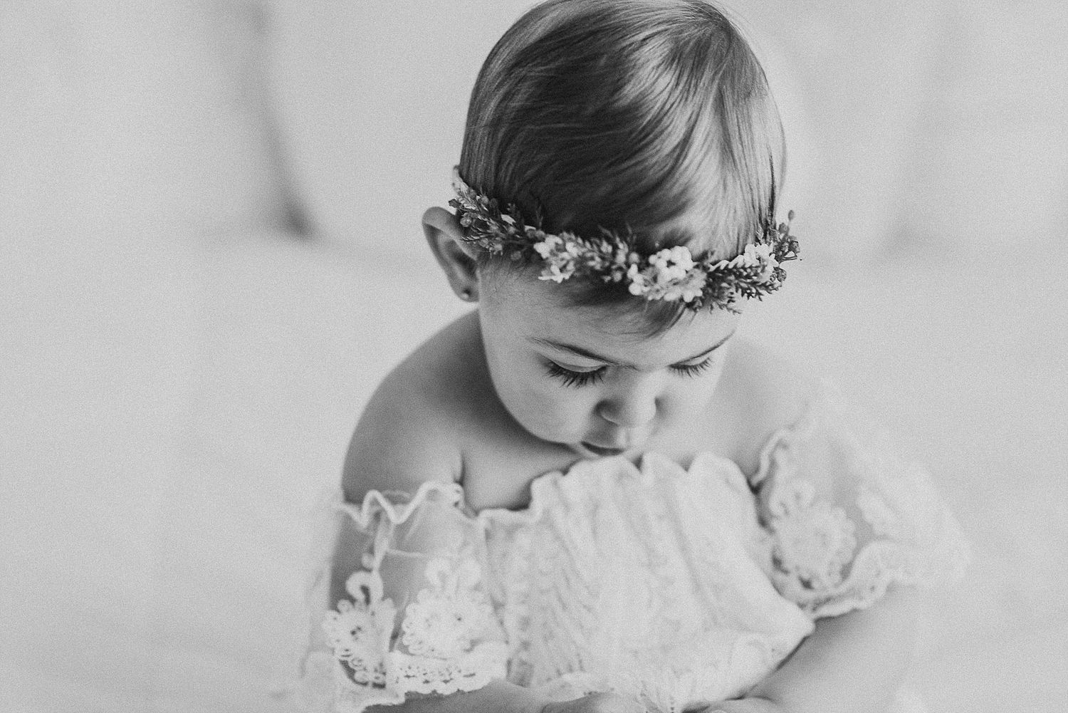 A black and white portrait of a small child wearing a delicate floral crown.