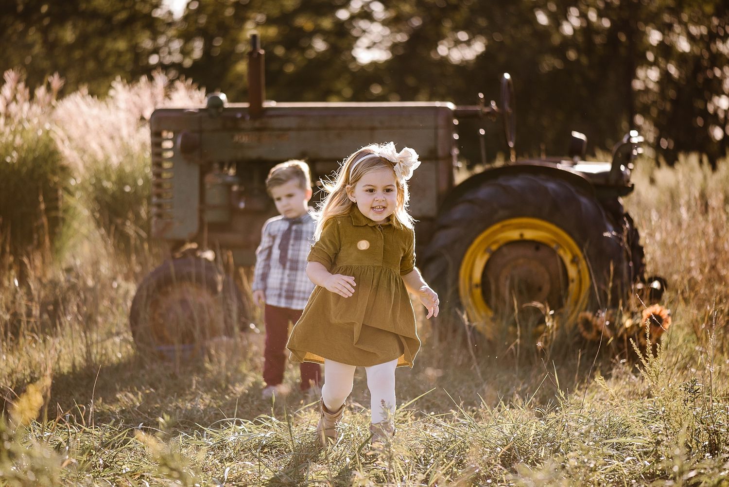Two children playing in a field at sunset with vintage tractor in background.