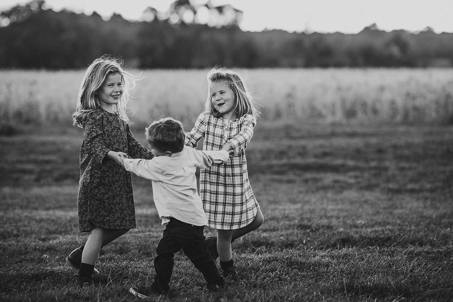 Three people holding hands in a circle dancing together in black and white.