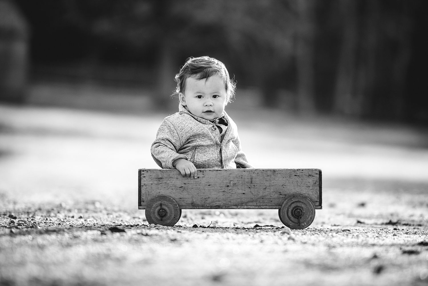 Small child sitting in wooden wagon outdoors in black and white photograph.