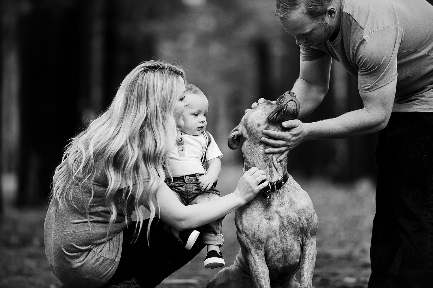 A black and white photo of people petting and interacting with a dog outdoors.