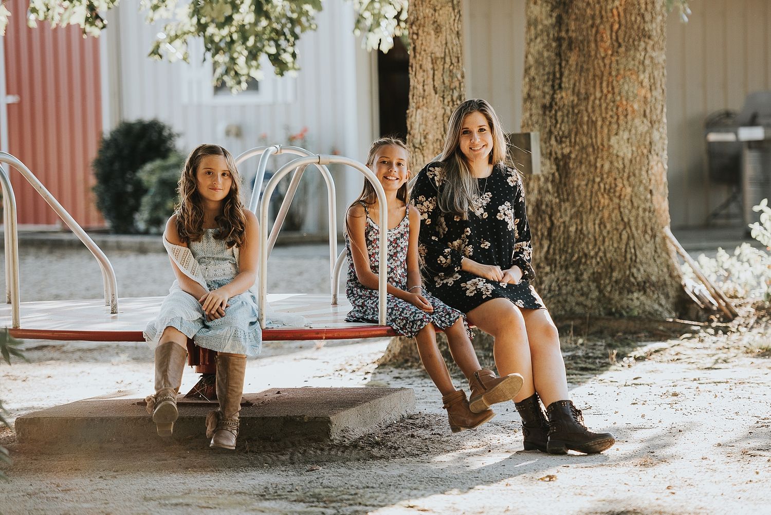 Three people sitting together on a bench under large trees on a sunny day.