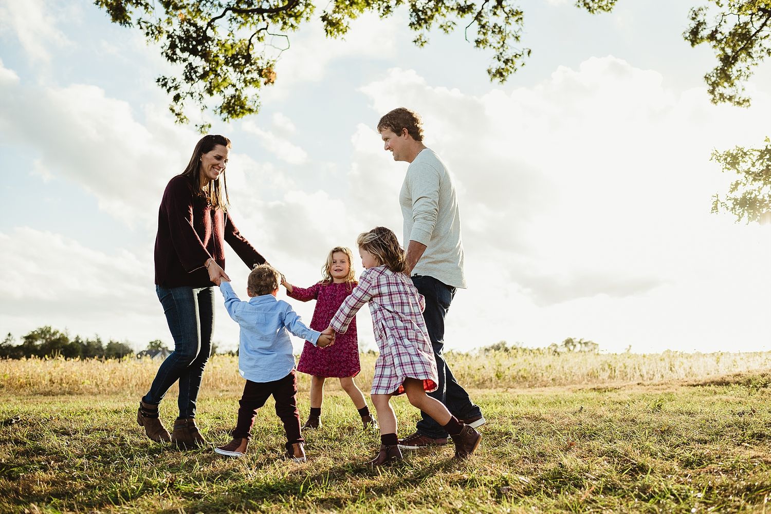 Family playing together in a sunny field with trees in the background.
