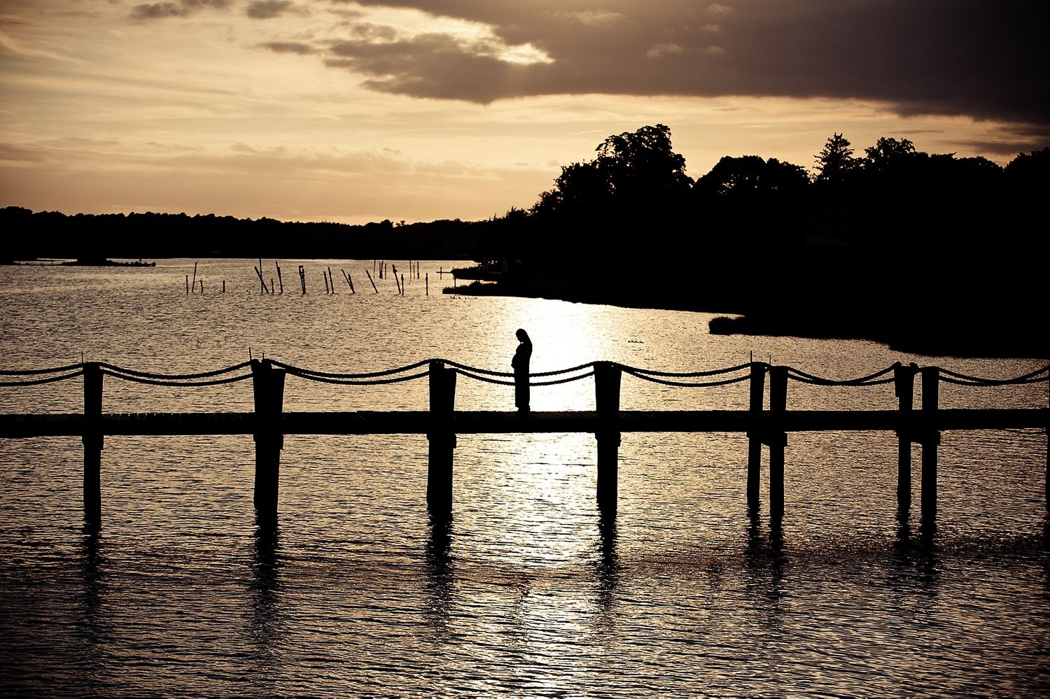 Silhouette of a person standing on a pier at sunset over a lake.