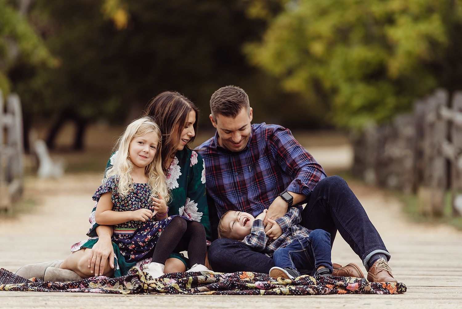 A family sitting together on a wooden boardwalk surrounded by autumn foliage.