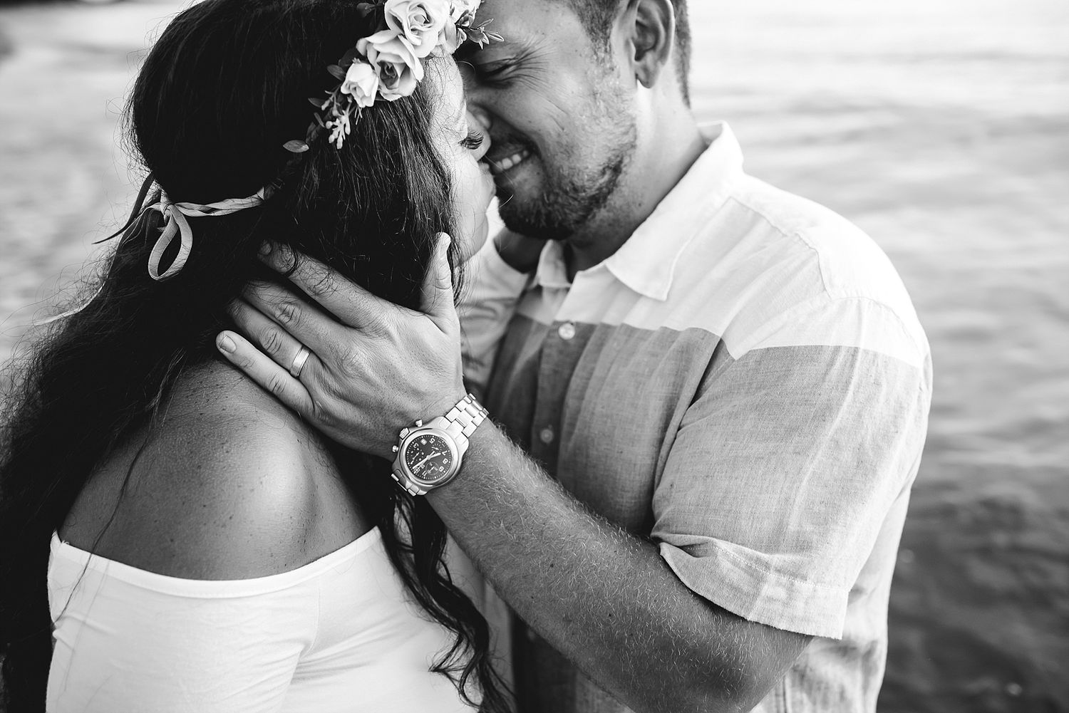 A romantic black and white portrait of a couple sharing an intimate moment by the water.