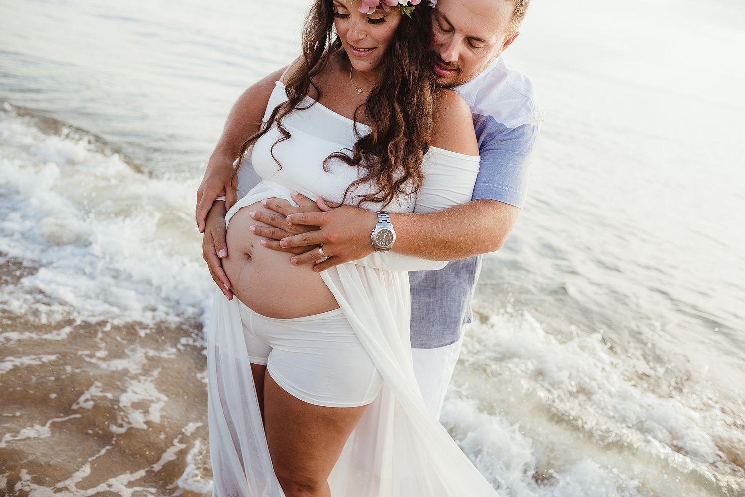 A couple embraces on a beach with waves lapping at their feet.