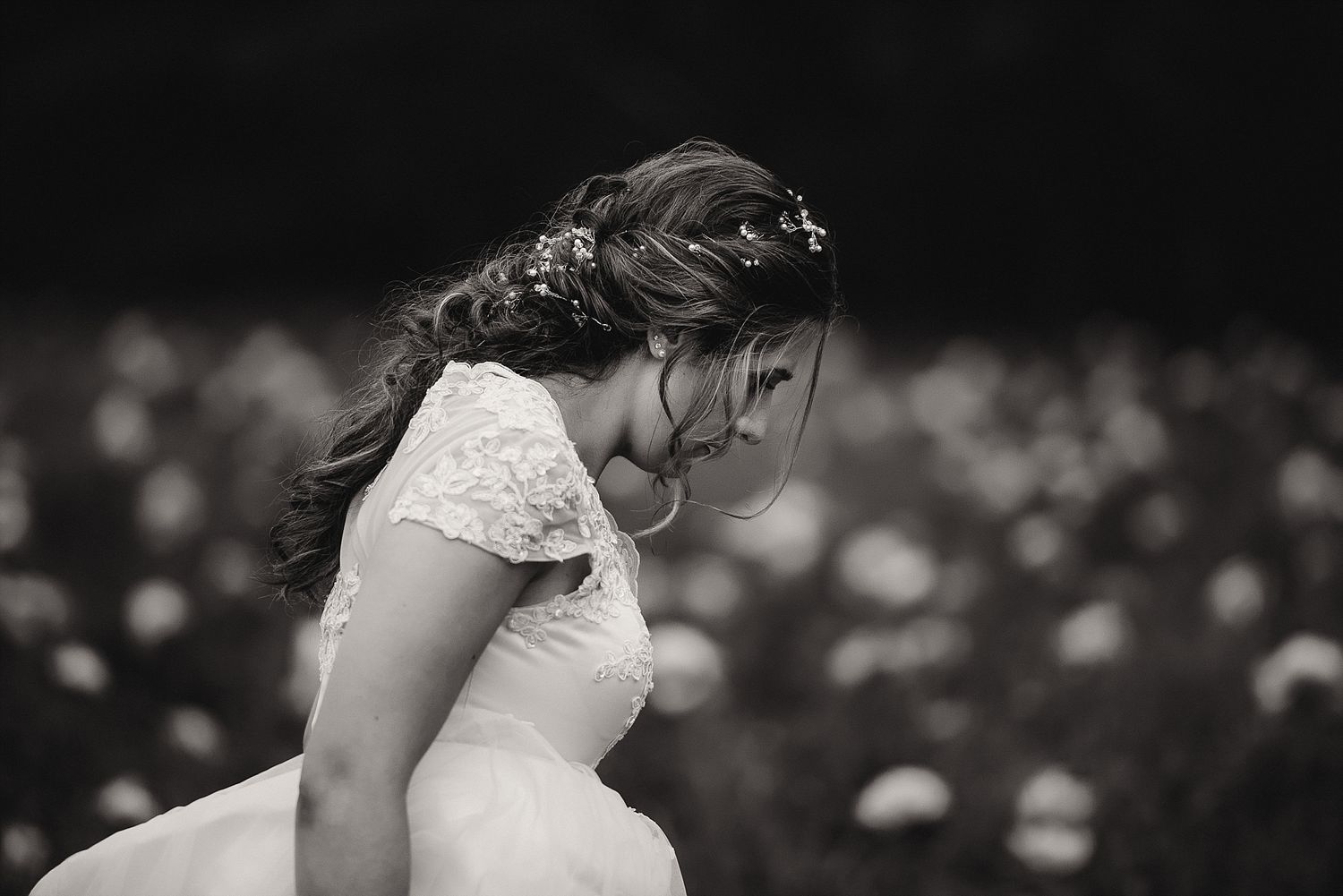 A black and white portrait of someone in a lace wedding dress looking down.