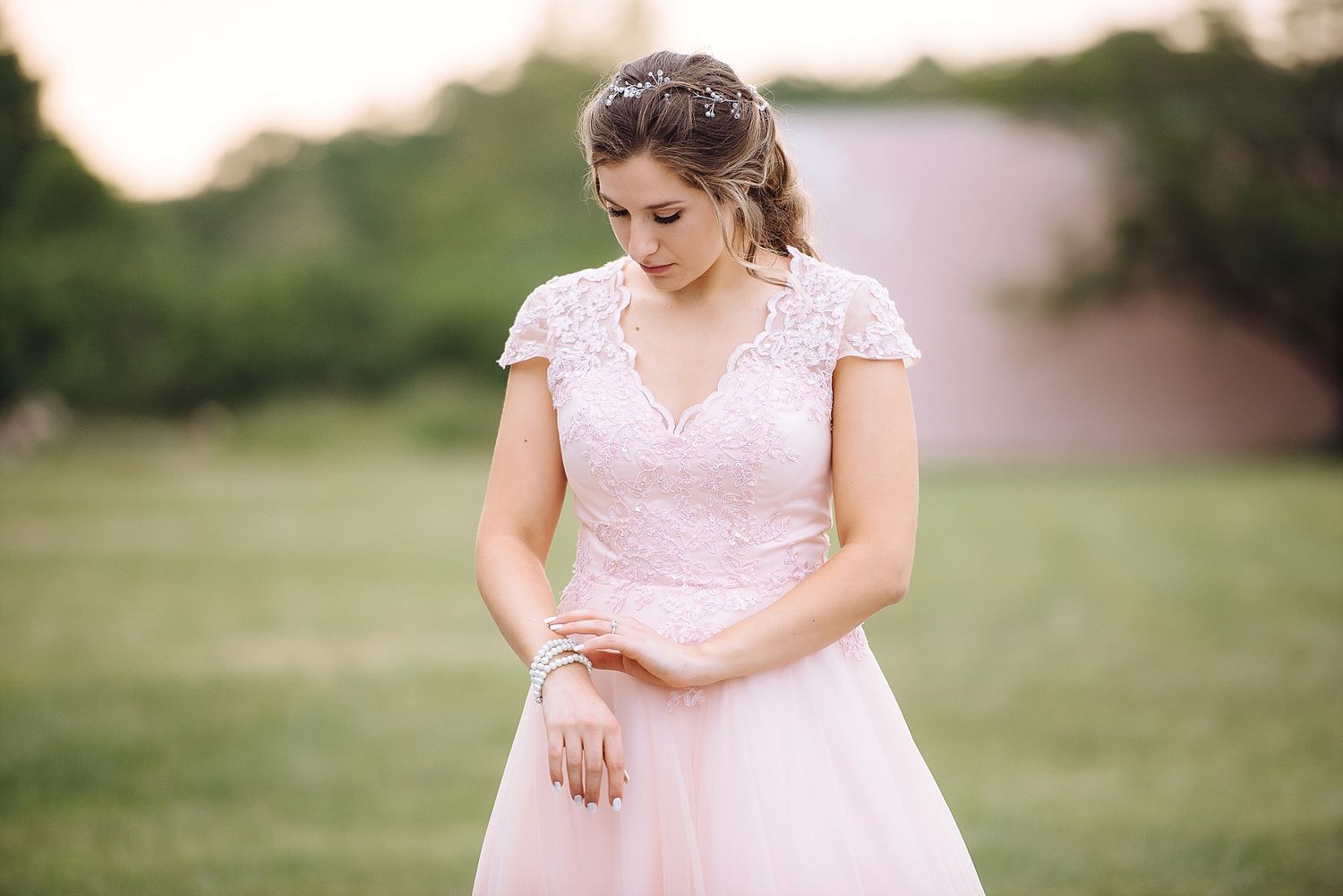 A bridal portrait featuring a soft pink lace dress in an outdoor setting.